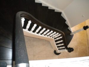 Das Foto zeigt eine schwarze lackierte Holz-Treppe mit Handlauf.