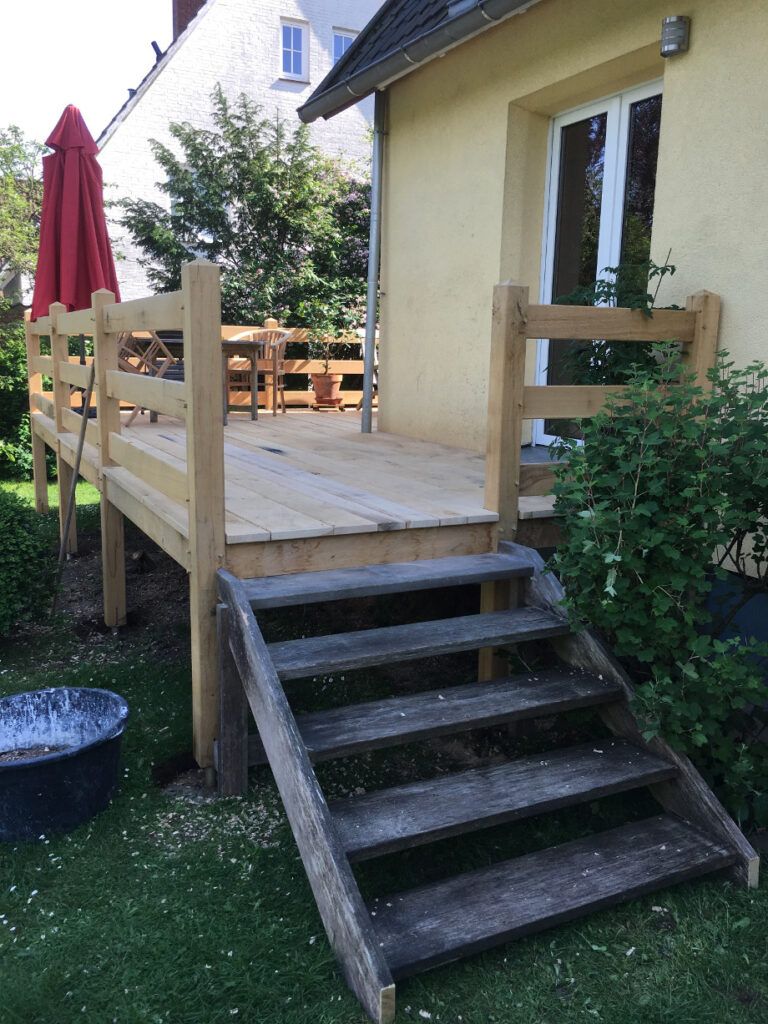 Das Foto zeigt eine Terrasse aus Holz mit einer kleinen Holz-Treppe als Aufgang vom Garten.